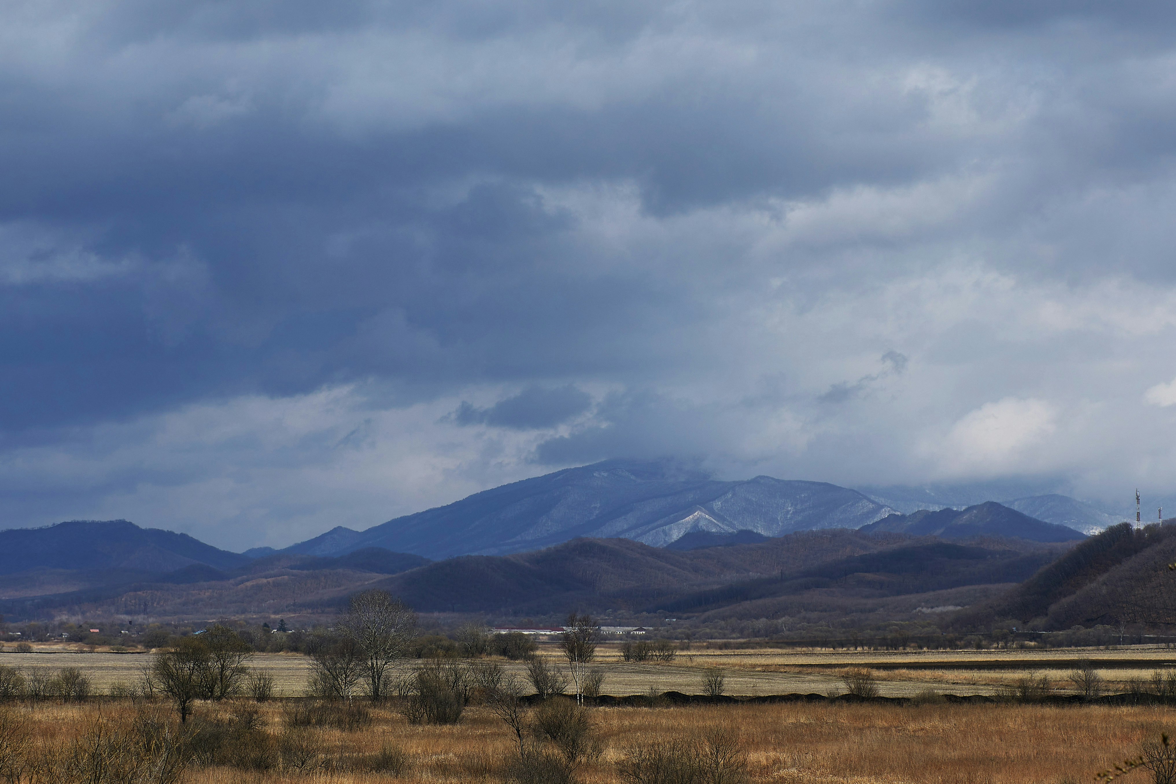 brown grass field near mountains under white clouds during daytime